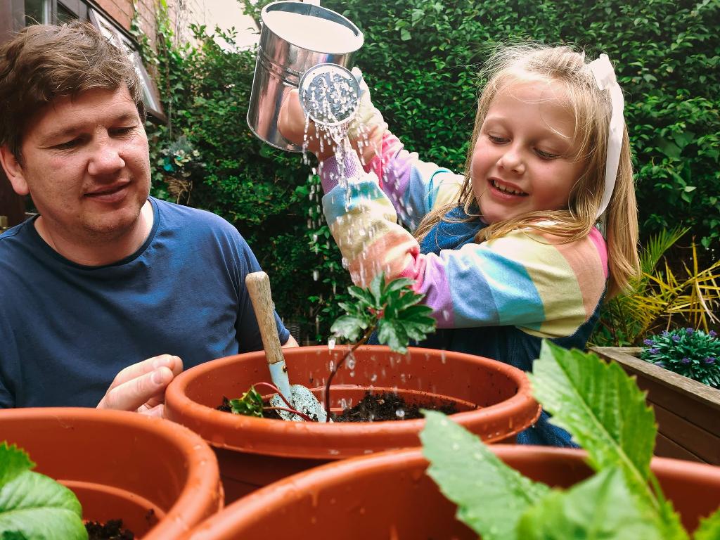Photo d'une enfant arrosant une plante accompagné d'un adulte la guidant pour le faire
