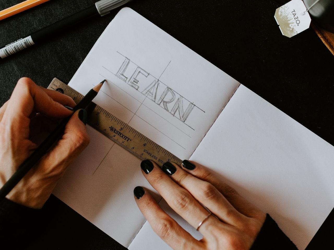 photo d'un cahier avec deux mains dessus sur lequel est écrit learn (apprendre en français)